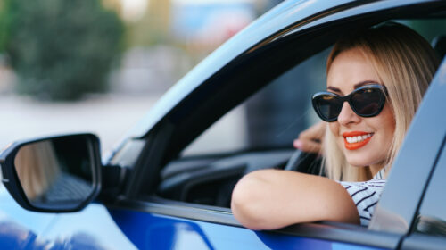 femme souriante avec des lunettes de soleil accoudé a la fenêtre de son véhicule